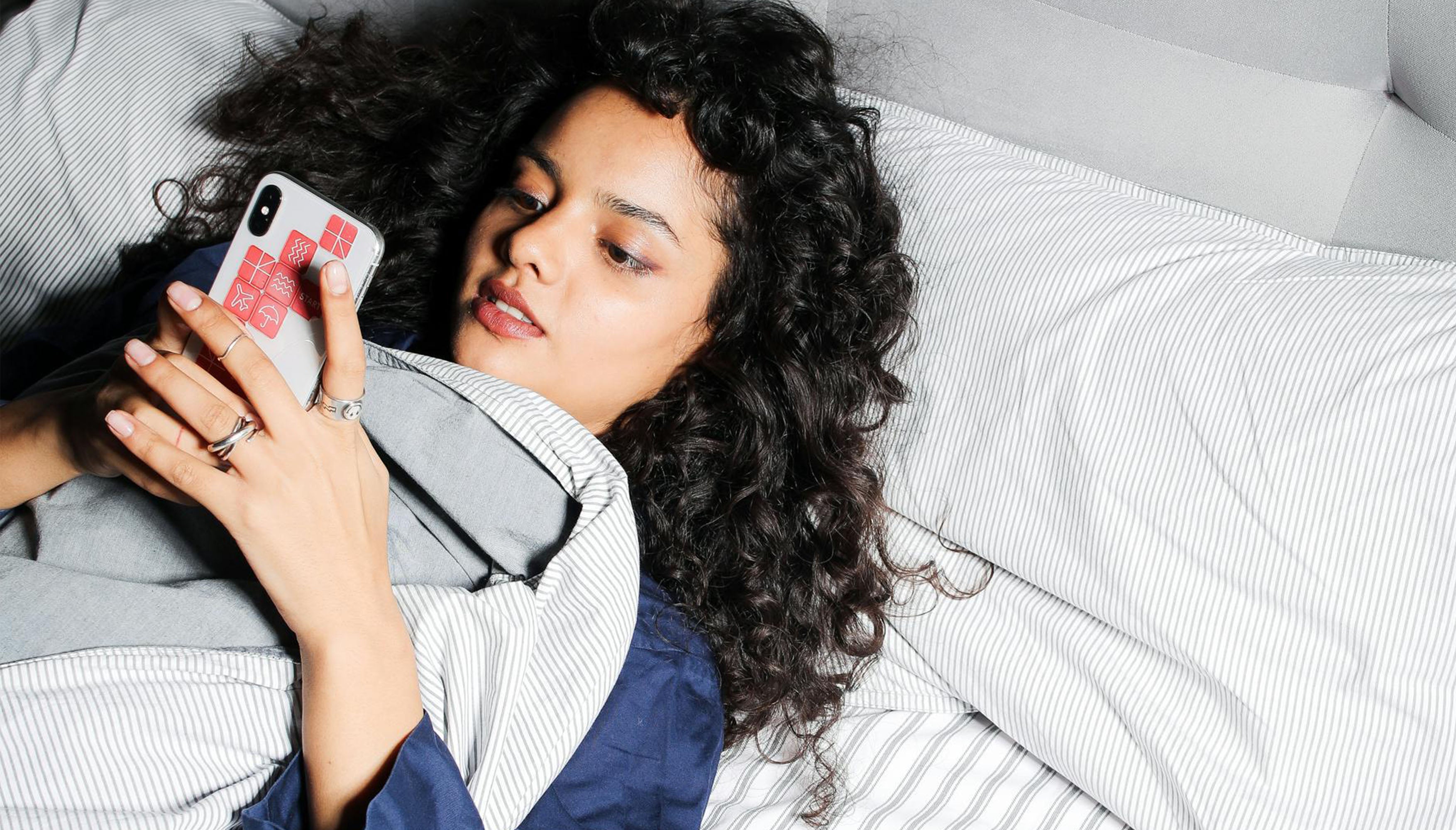 A woman looking at her cellphone while laying in bed