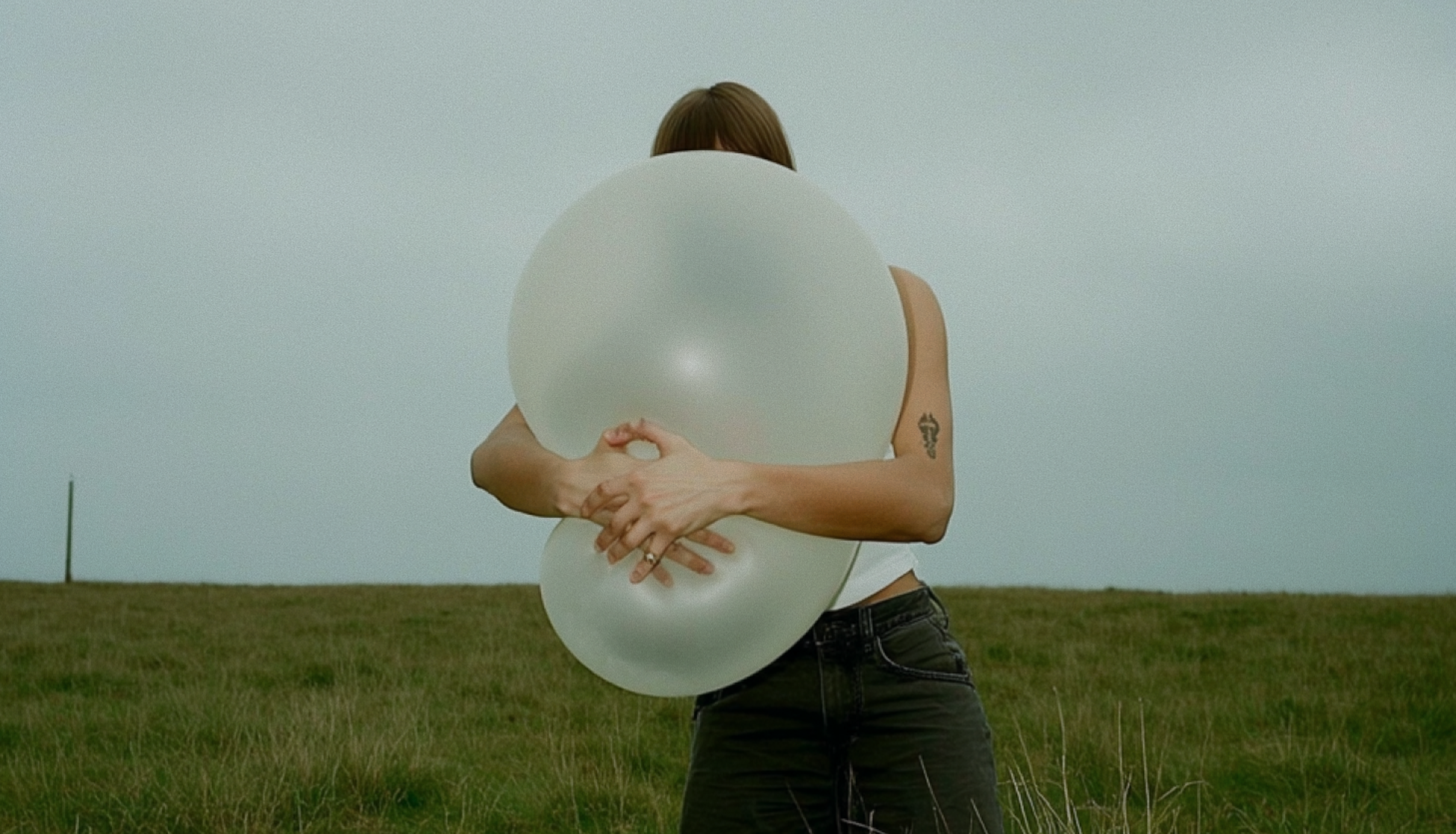 Person standing in a field with arms wrapped around a large inflated balloon and squeezing hard.