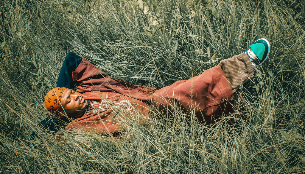 man in orange reclining in a flattened section of tall grass