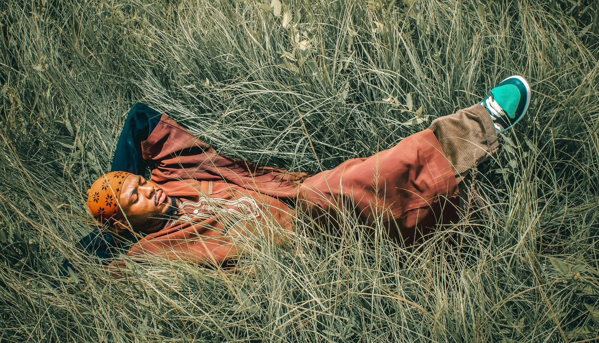 man in orange reclining in a flattened section of tall grass