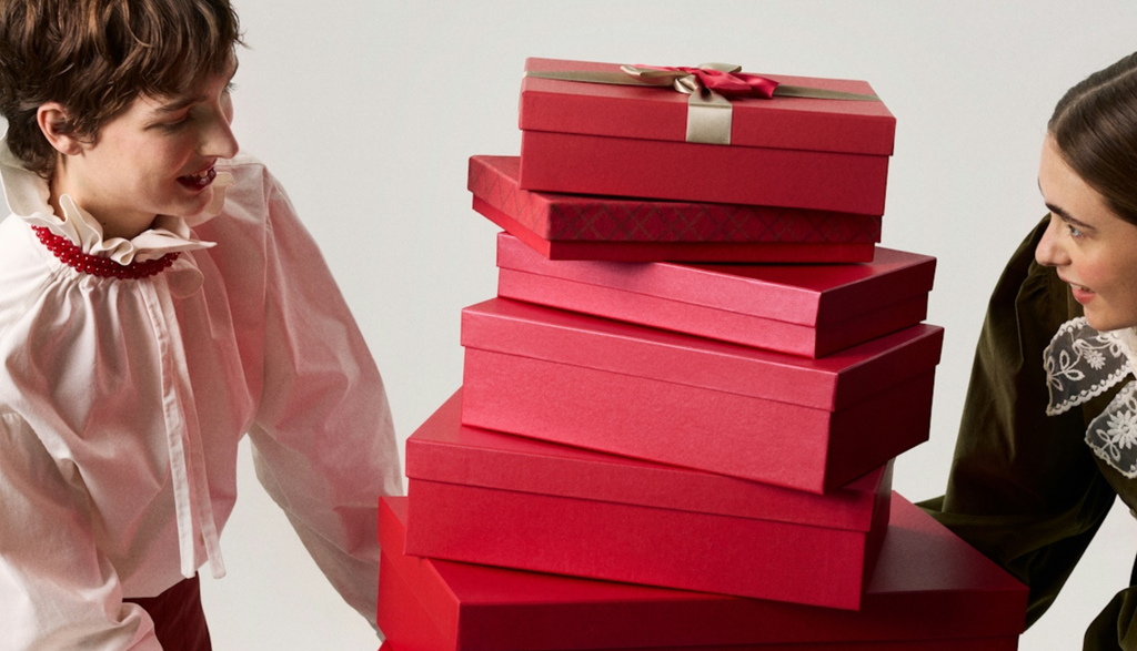 Two people marvelling at a tall stack of holiday gifts in red boxes that they have between them