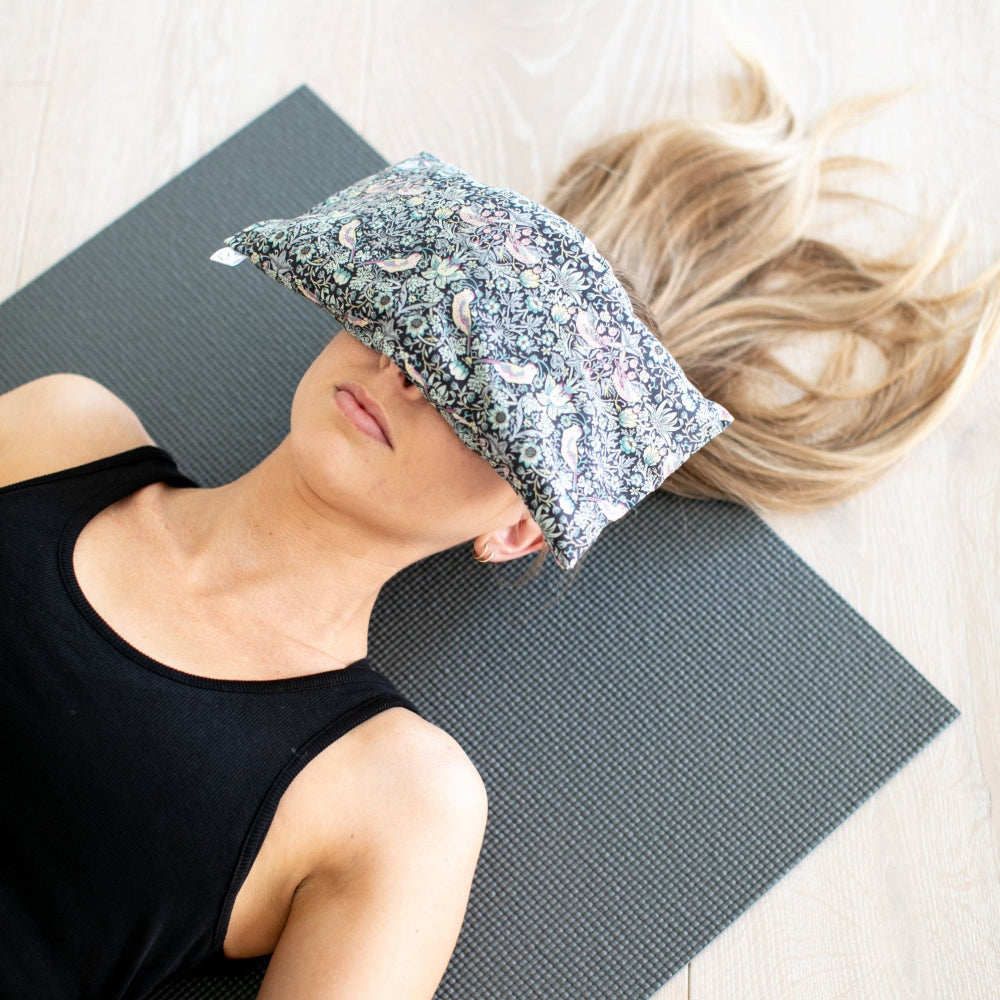 Person lying on a yoga mat with a floral eye mask on their face