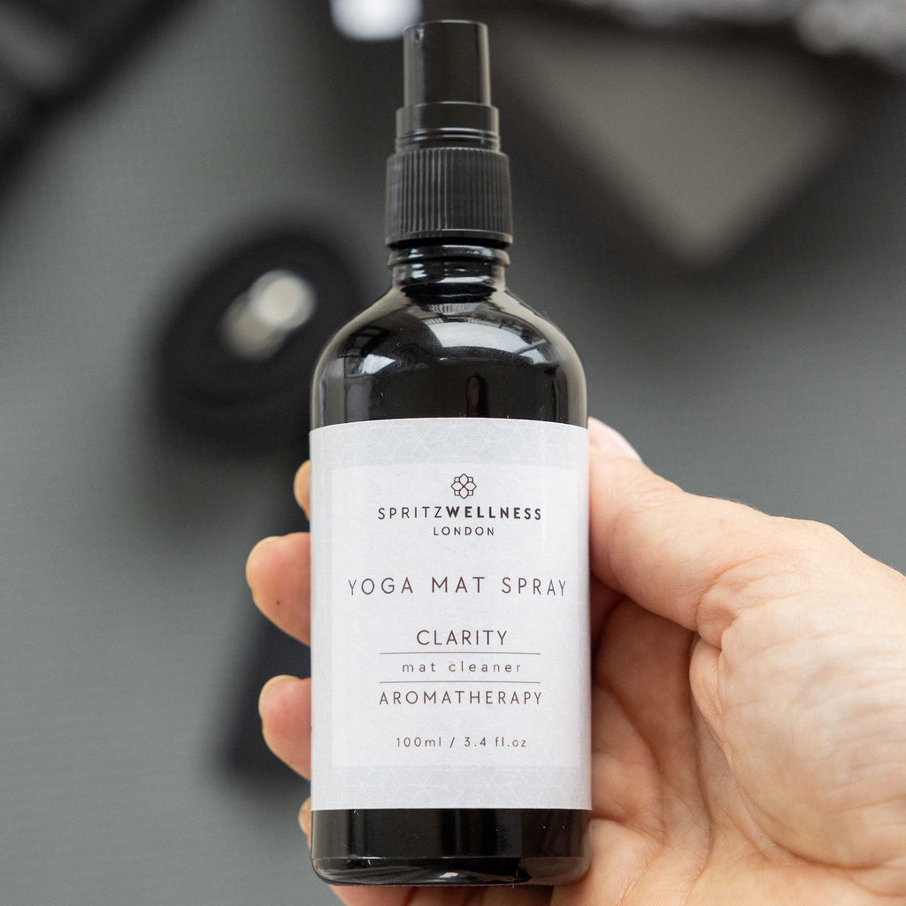 Hand holding a bottle of Spritz Wellness Clarity Yoga Mat Spray against a blurred background
